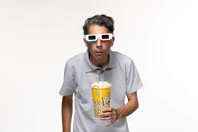 孤独正面图：年轻男性戴着d型太阳镜坐在白色桌子上吃爆米花青少年电影院衬衫