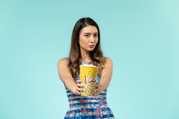 电影前视图年轻女性手持爆米花包在浅蓝色表面头发性感包装