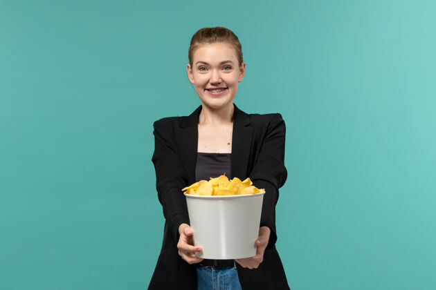 年轻女性正面图年轻女性吃薯片看电影 在蓝色的表面微笑电影院工人观看