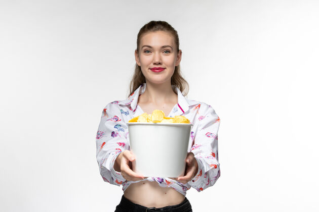 孤独正面图：年轻的女性拿着篮子 拿着薯片看电影 在白色的表面上微笑电影年轻女性电影