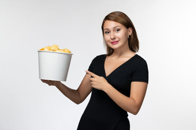 抱着正面图：年轻的女性拿着篮子和薯片 微笑着站在白色的表面上年轻的女性电影院篮子