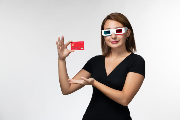 美丽正面图：手持银行卡的年轻女性戴着墨镜在白色表面微笑前面年轻女性太阳镜