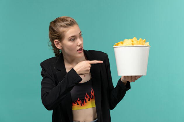 观看正面图：年轻的女性拿着薯片在蓝色的水面上看电影年轻女性电影杯