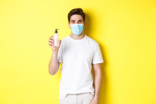 面膜covid-19的概念 检疫和生活方式戴着医用口罩的年轻人展示洗手液 手消毒产品 站在黄色背景上男性面膜模特