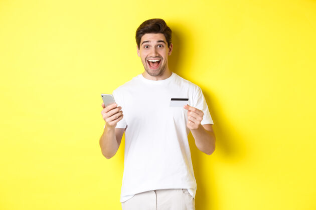 男人快乐男买家手持智能手机和信用卡 网上购物的概念 站在黄色背景下模特黄色帅哥