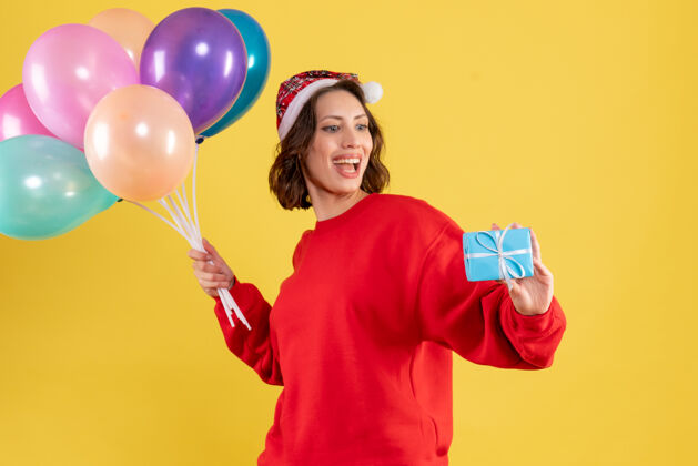 情感正面图年轻女子手持气球和小礼物在黄色圣诞假期新年感慨女人女人年轻女人气球