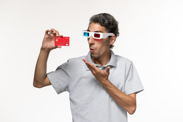 手持正面图年轻男子手持红色银行卡 戴着d墨镜 在白色表面遥控前太阳镜
