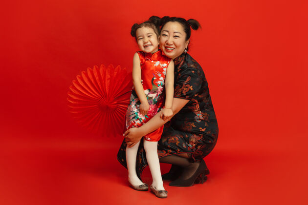 中国穿着传统服装的亚洲母女肖像被隔离在红墙上文化中国新年欢呼