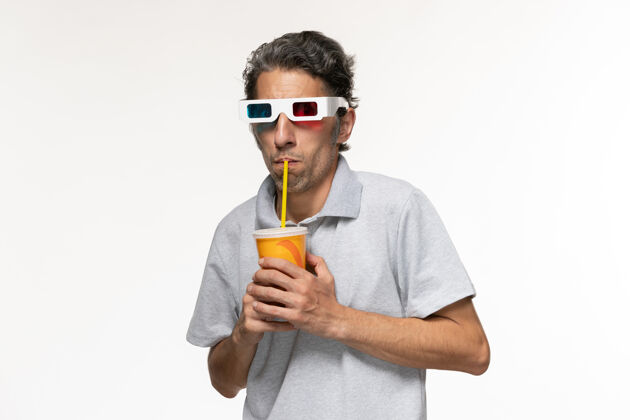 电影正面图：年轻男性戴着d型太阳镜在白色表面上喝苏打水看电影男性苏打水孤独
