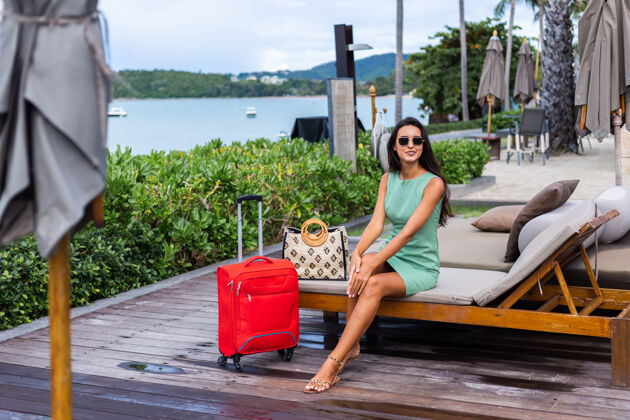 度假快乐的白种人漂亮的长发优雅的旅游女人在酒店外面穿着红色的手提箱优雅时尚行李