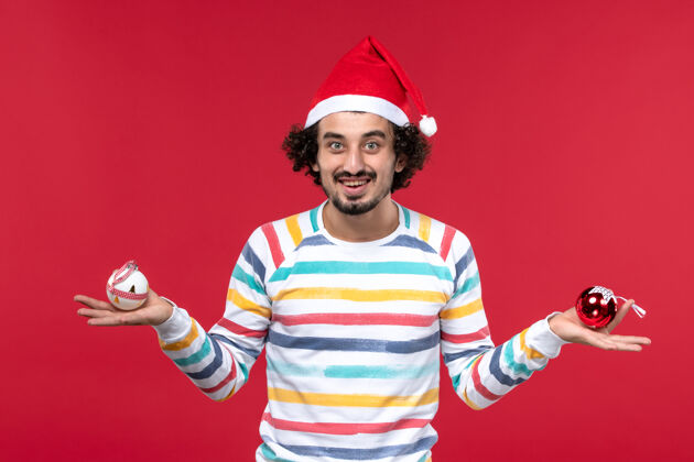 圣诞节正面图：年轻人拿着塑料玩具微笑着站在红墙上人类节日新年红微笑玩具人