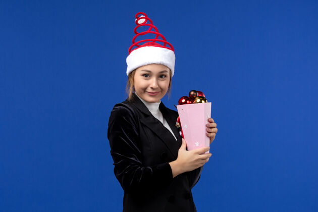 西装前视图年轻女性手持圣诞树玩具 背景为蓝色新年假期情感色彩年轻女性颜色看法