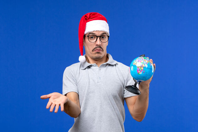 圣诞节正面图年轻男性手持地球仪在蓝墙飞机上度假男性之旅世界足球球员