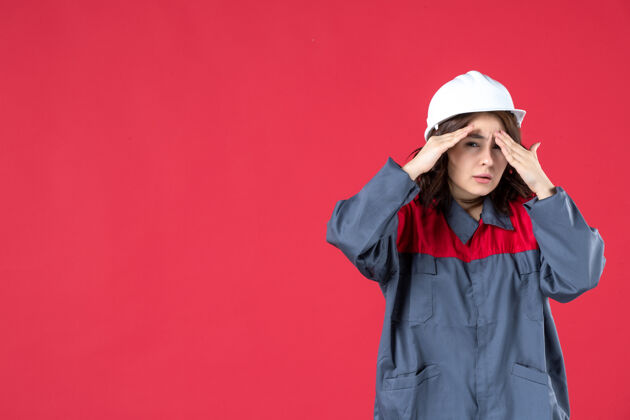 工程师在孤立的红墙上 穿着制服 戴着安全帽的惊讶的女建筑工人的特写镜头人女建设者惊喜
