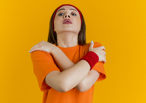 肩令人印象深刻的年轻运动女性戴着头带和腕带 双手交叉放在肩膀上 隔离在橙色墙壁上 留有复制空间女士橙色年轻