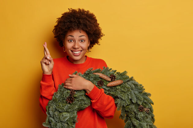 青年准备寒假和节日的室内装饰快乐的非洲裔美国妇女交叉手指 许愿 摆圣诞花圈房子情绪卷发