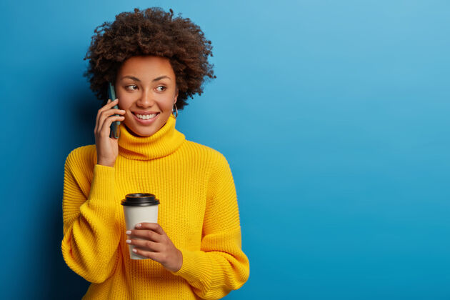 黑发快乐无忧无虑的女人一边喝咖啡一边用手机聊天 穿着黄色毛衣人女人咖啡