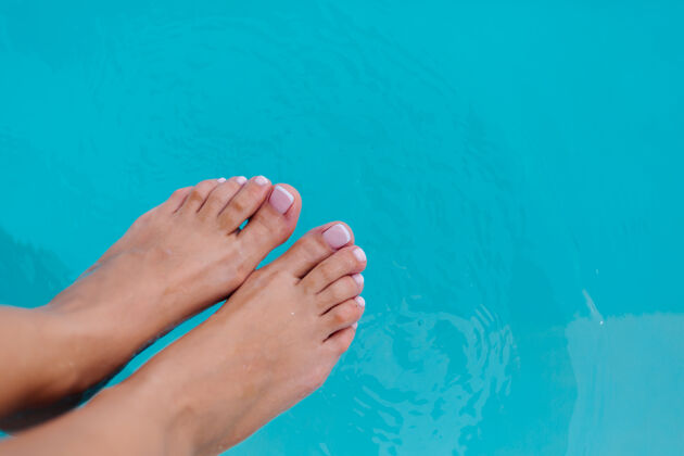 白在游泳池蓝色海水的背景下 用法国足疗凝胶上光剂来结束女性的足部秀漂亮晒黑蓝