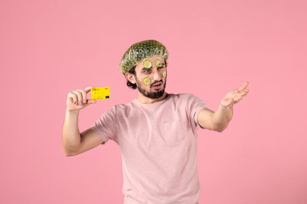 黄瓜正面图：戴着面具的年轻男子 手持粉色背景的银行卡脸男性持有