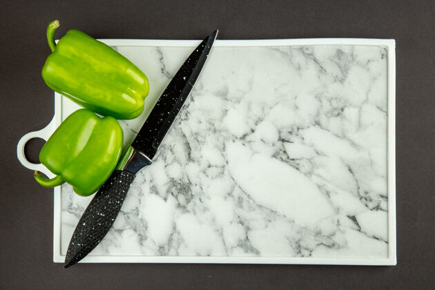 素食黑色表面上有绿色甜椒的白色砧板俯视图营养甜椒食物