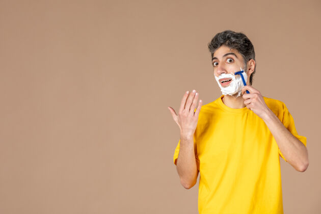 淋浴正面图：年轻男性在粉色背景上剃着泡沫脸身体护理肖像视图