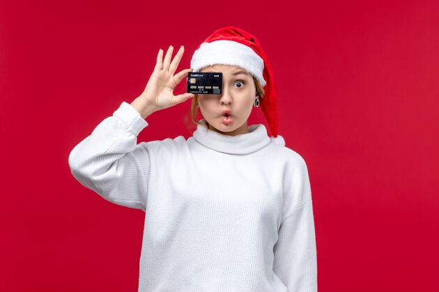 持有正面图年轻女子拿着银行卡在红色的地板上红色的节日圣诞钱银行人卡片
