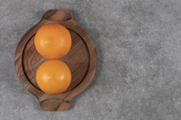 特写灰色桌子上方木制托盘上两个成熟的橙子的俯视图自然组黄色