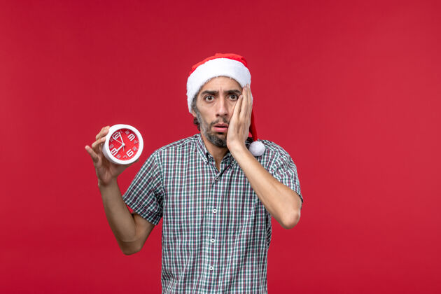 成人正面图红色背景上手持圆形时钟的年轻男性男人情绪前面