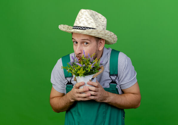 花盆令人印象深刻的年轻英俊的斯拉夫园丁制服和帽子举行花盆看起来孤立的绿色墙壁与复制空间制服印象拿着