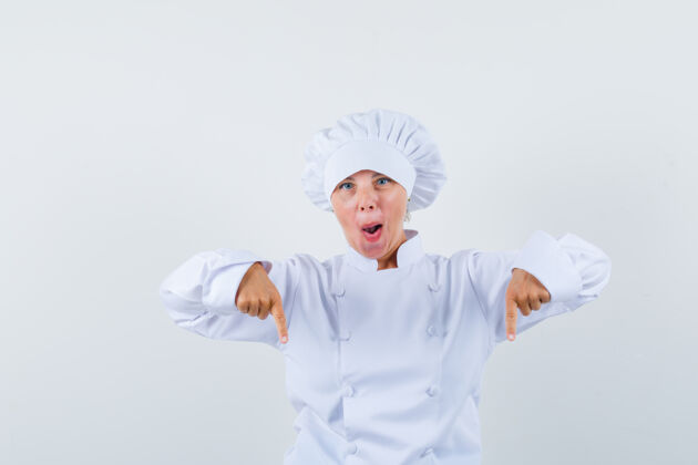 模特一位身穿白色制服的女厨师指着下面 看上去很惊讶厨师年轻时尚