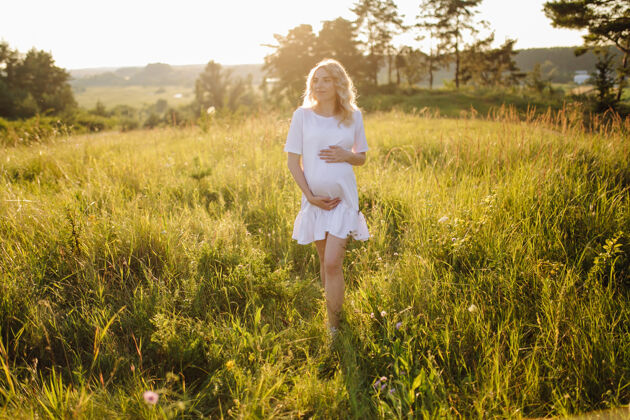 户外带着夕阳在公园里散步的孕妇绿色春天怀孕