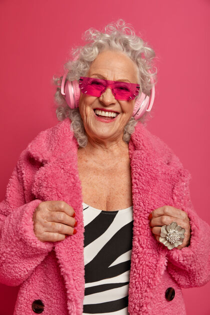 享受穿着粉色紧身衣和外套 满脸皱纹的时尚老奶奶的特写照片耳机乐趣人物