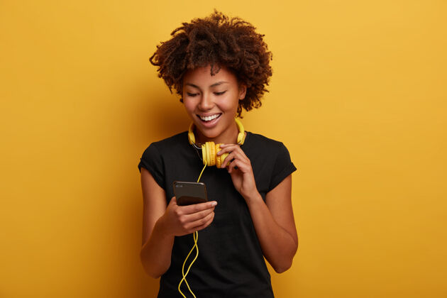 肖像快乐的卷发女孩拿起播放列表中的歌曲 脖子上戴着黄色耳机青少年耳机音乐
