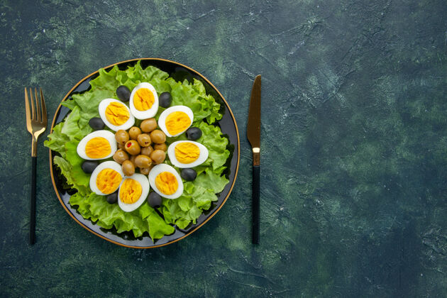 茶俯视图深蓝色背景上的煮熟切片鸡蛋 橄榄和绿色沙拉沙拉菜早餐