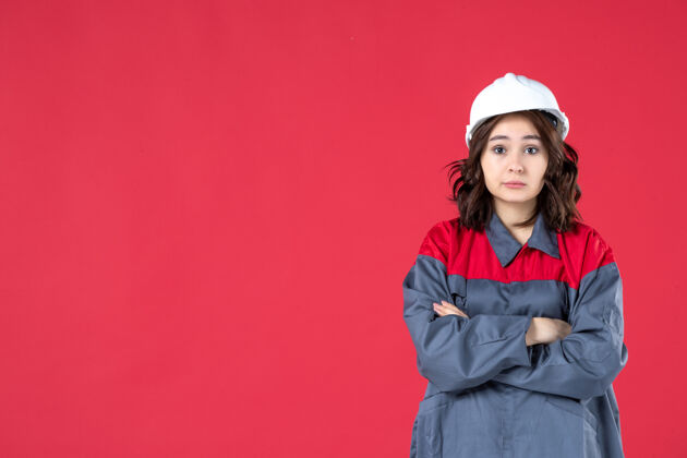 女士正面近距离拍摄的是一位穿着制服 戴着安全帽的女性建筑工人 她双臂交叉在隔离的红墙上人人成人