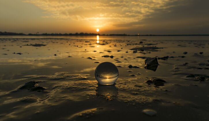 岩石日落时拍摄的海滩上透明小球的迷人景色云夜晚海洋