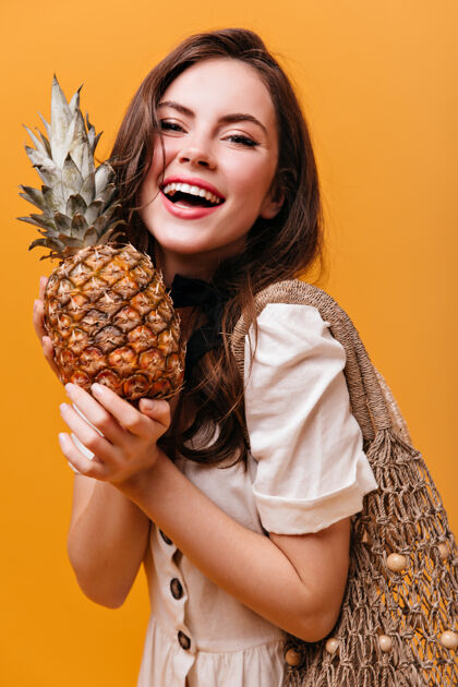 化妆品照片中的黑发女孩心情非常好 手里拿着菠萝和橙色背景上的线袋菠萝橙色背景肖像