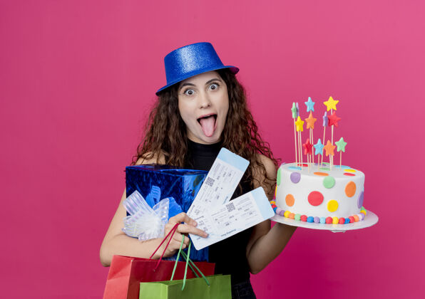 机票年轻漂亮的女人 卷发 戴着节日礼帽 手里拿着生日蛋糕礼盒和机票 疯狂的生日快乐派对概念超过粉色抱着疯狂派对