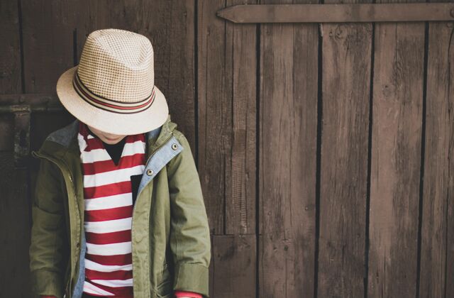 上衣一个穿着绿色外套 条纹衬衫和帽子的小男孩在木制背景上的特写镜头衣服表情外面