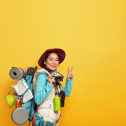 寻找活跃的女游客做出和平姿态 手持复古相机拍照 背着大背包 里面有目的地地图 卡雷马特等旅游用品复制空间旅行度假