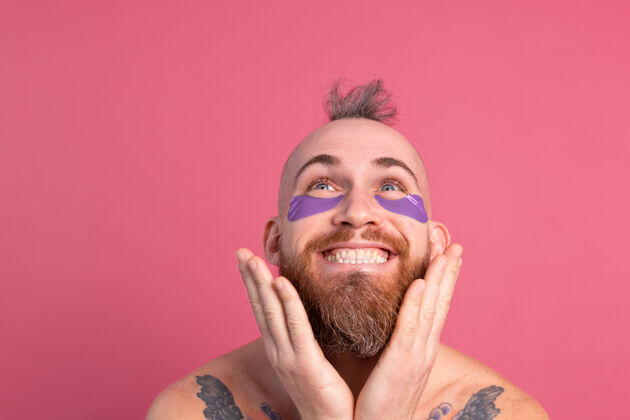 胶原蛋白欧洲帅哥留着胡子纹身上身的男人戴着紫色眼罩对着镜头摆粉红色的姿势卫生空虚欢呼