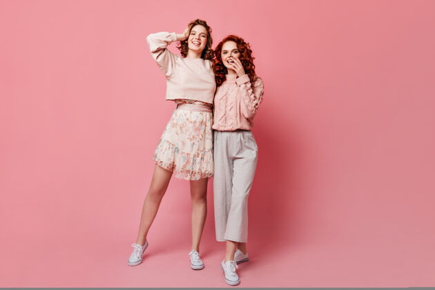 情绪穿着裙子的女孩与朋友合影的全貌两位时尚的年轻女士站在粉色背景上的摄影棚镜头爱情微笑在一起