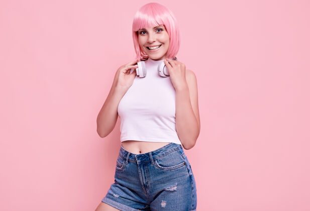 Dj美丽明亮的潮人女孩的肖像与粉红色的头发享受音乐在耳机上五颜六色声音漂亮发型