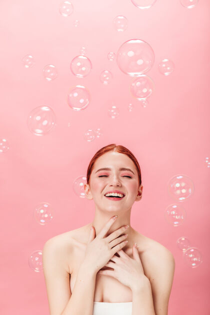 肥皂泡正面是一个充满肥皂泡的快乐的姜黄色女人迷人的白人女孩在粉色背景下独自大笑孤立的粉红色粉色微笑