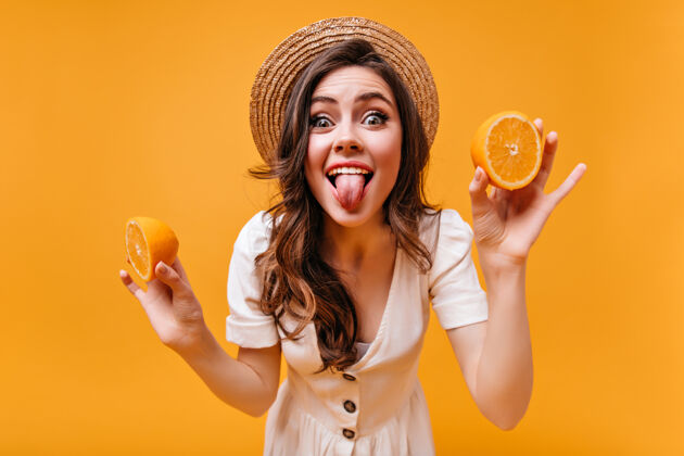 波浪发活泼的女孩戴着帽子 穿着夏装 露出舌头 摆出橘子的姿势脸化妆微笑
