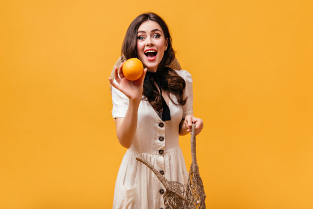 橙色一位身穿白色套装 脖子上系着黑色蝴蝶结的年轻女子从线袋里掏出橘黄色的衣服包脸连衣裙