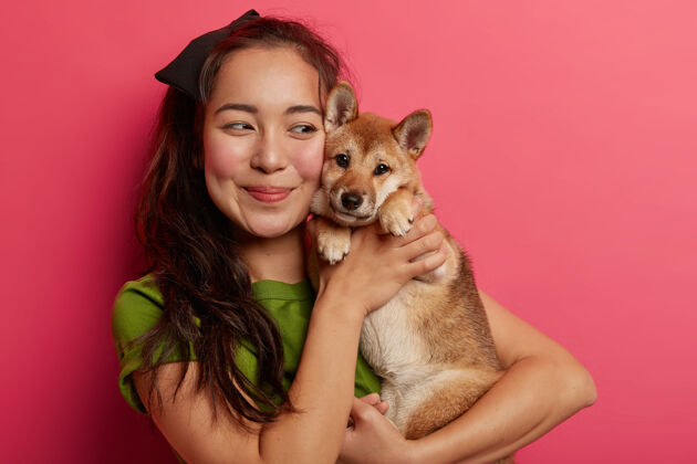 亚洲可爱的韩国女孩爱上了她的shibainu狗 微笑着拥抱宠物 深色头发 穿着绿色t恤 在粉色背景下与动物合影女性拥抱看