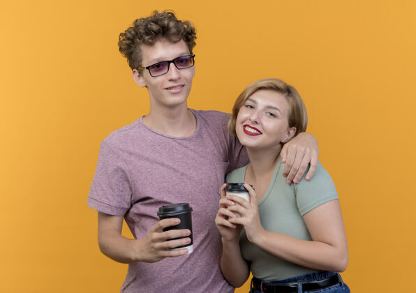 男人一对年轻漂亮的情侣 穿着休闲服 手里拿着咖啡杯 脸上挂着橙色的笑容微笑女人衣服