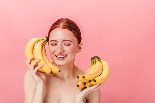 女孩放松的欧洲女人拿着成熟的香蕉姜色迷人的女孩摆出异国水果隔离在粉红色背景上前视图香蕉情感