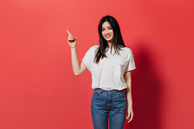 亚洲人穿着牛仔裤的可爱女人在红墙上展示手指放置文字粉色情感跳跃